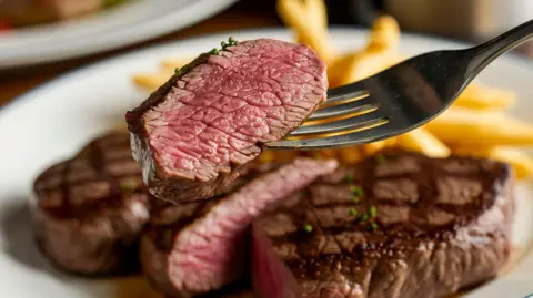 Appetising close up of a rare-cooked steak, with a fork lifting one mouthful