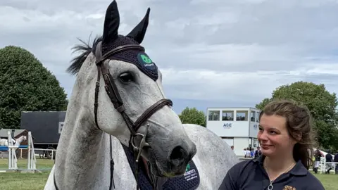 Stephanie Nelson/BBC A woman dressed in a dark polo shirt gazes into the eyes of a horse in a paddock at the Royal Norfolk Show