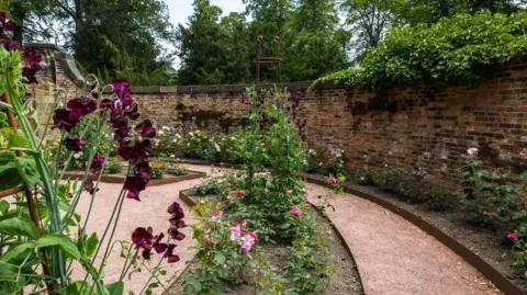 Wentworth Woodhouse Preservation Trust Part of a circular walled garden. Flowers are in the foreground and background, while a path winds round the area close to a high wall.