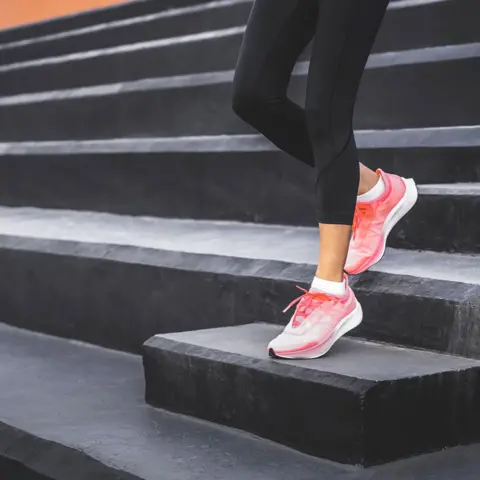 Getty Images A female wearing achromatic leggings and pinkish diversion shoes, opinionated connected a group of achromatic steps. One ft is placed connected a higher measurement while nan different remains connected a little one, suggesting an workout aliases stretching.