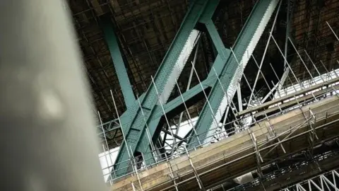 Restored section of the Tyne Bridge showing scaffolding and the structure's heavily riveted lower west arch, freshly painted in the shade Hollybush Green.