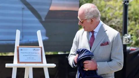 King Charles III unveils a plaque to officially launch the new UK Space Agency (UKSA) observatory. He turns to face the plaque while holding the cover