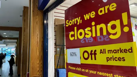 A large closing down sign in the window of a shop. The sign is red with yellow writing saying 'Sorry. We are closing! 60% of all marked prices".