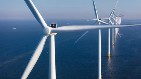 Stock image of offshore wind turbines - tall, windmill-like structures rising from the sea.