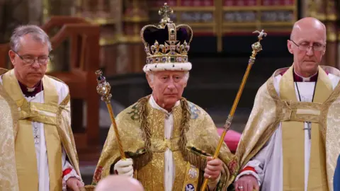 Inside the abbey, King Charles wears a jeweled crown, golden robes and holds two golden scepters.