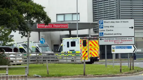 Ambulances parked outside the emergency department at Crosshouse Hospital. A sign next to the ambulance bays directs drivers to different car parks and units