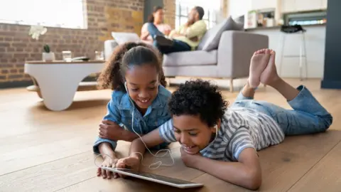 Getty Images Happy children at home watching videos on a tablet computer using headphones and smiling