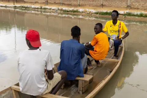 CHANCELIN MBAIRAMADJI MOITA/EPA Orang-orang menggunakan perahu untuk bergerak di jalan yang banjir.