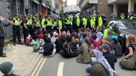 People sitting on the street in front of police.