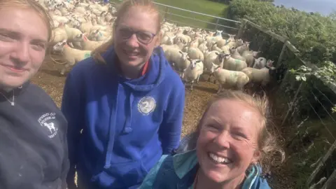 ANNA KERRUISH Anna with two colleagues in a pen with a flock of sheep behind them.