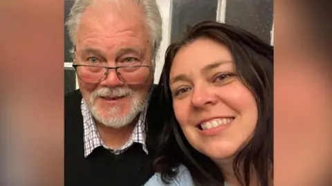 Emma Herrick Emma Herrick (right) with long dark brown hair wearing a pale blue top takes a selfie of her and her dad, Roy, who has grey hair and glasses and is wearing a checked shirt and black jumper. They are both smiling.