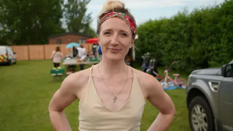 BBC/Shaun Whitmore A woman with a cream top and colourful hairband - standing outside at a car boot sale