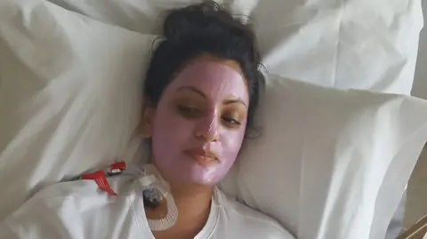 JASLEEN KAUR CARROLL Jasleen in a hospital bed with a tube inserted into her neck.