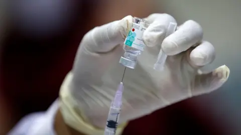 A health worker prepares a Human Papillomavirus (HPV) vaccine during a vaccination programme. They are wearing a white medical glove and the vial of vaccine and syringe can be seen in close up.
