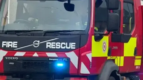 A fire engine driving towards the camera with the blue lights on its dashboard illuminated