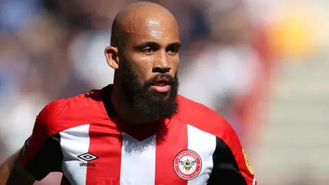 Bryan Mbeumo wears a red and white striped Brentford shirt during a football match