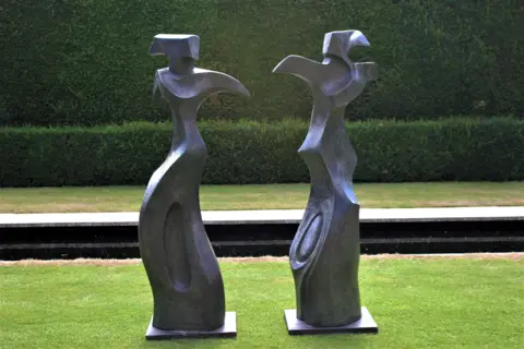 Art for Cure Two angular figures stand on a neat lawn
