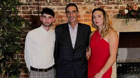 Supplied Russell wearing a suit standing alongside Kayleigh in a red dress