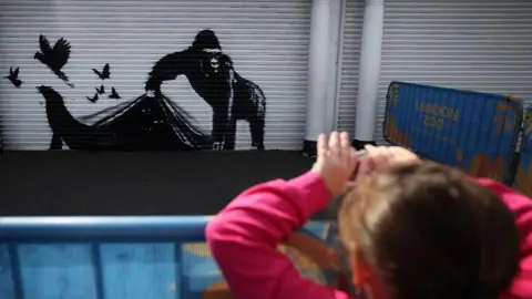 EPA Someone photographs Banksy's artwork depicting a black gorilla on a silver metal shutter