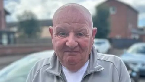 Pat Jamieson wearing a tracksuit jacket and white t-shirt stands on a street in Tollcross.