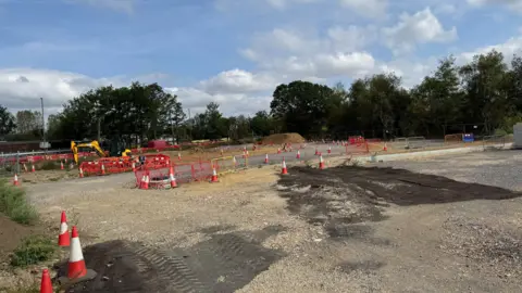 Cones and red fencing litter a barren construction site. 