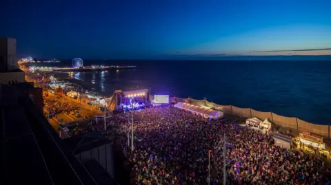 Blackpool Council Thousands of people pack Blackpool Promenade as the sun sets over the sea.