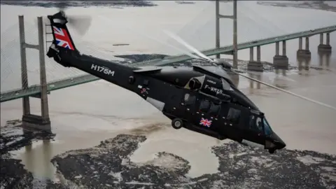 Airbus A black Airbus helicopter flying over a body of water and a bridge