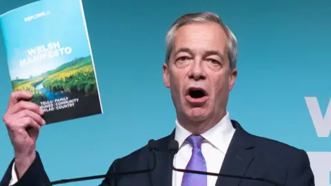 Reform UK leader Nigel Farage at the Reform UK manifesto launch for the Senedd elections in May, at the International Convention Centre Wales in Newport. He holds up Reform's manifesto