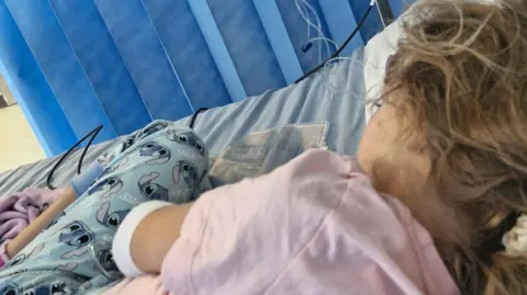 Collect/PA Real Life A young female child, Ruby, is a hospital bed wearing Lilo and Stich pyjamas