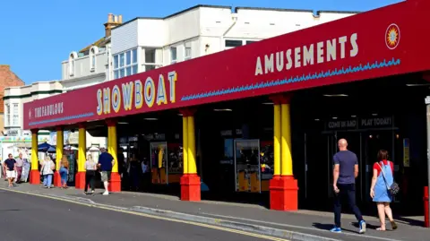 Getty Images People walk past a seafront arcade with red sign and yellow pillars.