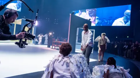 Tristram Kenton Press photograph of Angel's Bone at the Aviva Studios in Manchester. The image shows the cast on stage, a mobile camera and a giant screen in the background. 
