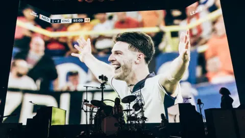 Chris Phelps Big screen showing England's Declan Rice celebrating, with drum kit in the foreground