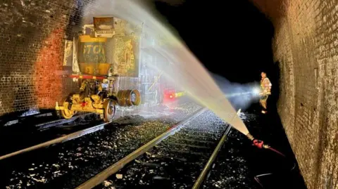 West Yorkshire Fire and Rescue A maintenance vehicle in Standedge Tunnel being hosed down by firefighters wearing protective clothing 