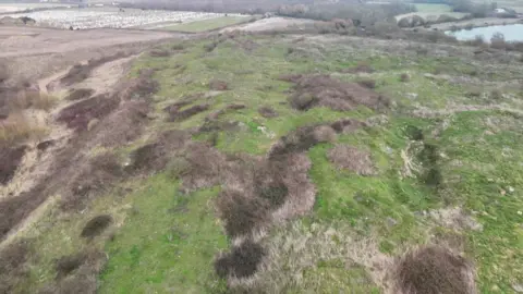 A bumpy landfill site with overgrown foliage seen from the air