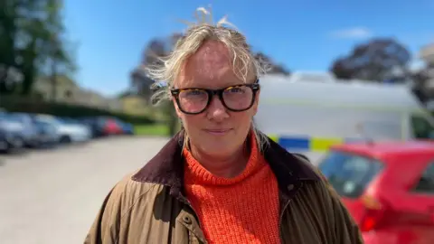 Jemma Young who lives on the road, looking at the camera. She is wearing an orange jumper and glasses