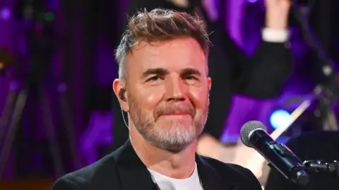 Getty Images Barlow sat at a piano as an adult. He wears a black jacket and white shirt and has short hair and stubble.