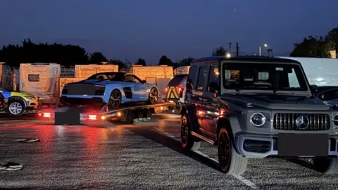 Avon and Somerset Police A light blue supercar shown being towed away on a trailer in a car park. 