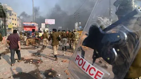 Getty Images Riot Police walks along a road spread with stones after clashes between supporters and opponents of the new citizenship law, in the bhajanpura area in New Delhi on February 24, 2020.