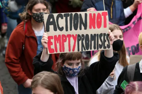 PA Media Climate change protestors wearing facemasks taking part in a protest march with one holding a homemade banner that reads action not empty promises.