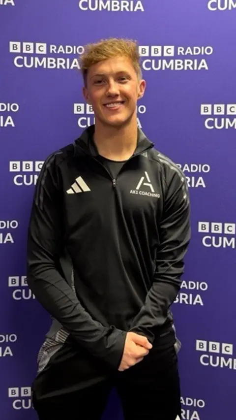 Thomas Atkinson standing in front of a purple BBC Cumbria board