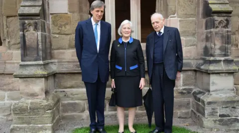 L-R: The Lord-Lieutenant of Herefordshire Mr Edward Harley, with two former Lord-Lieutenants for the county -  the Dowager Countess of Darnley, and Sir Thomas Dunne. They are standing outside a cathedral building and dressed formally, wearing suits.

