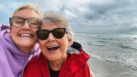 A smiling mother and daughter posing for a selfie at the seaside