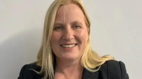 Michelle Haywood, who has long light coloured hair and is smiling. She is wearing a black jacket.