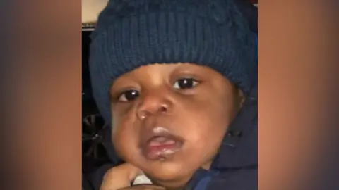 Bedfordshire Police The close-up image of a young boy. He is a few months old. He has big brown eyes and is wearing a navy coat.