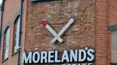 Handout A photo of the outside of a red brick building with two crossing matches and a Moreland's sign on the side of the wall