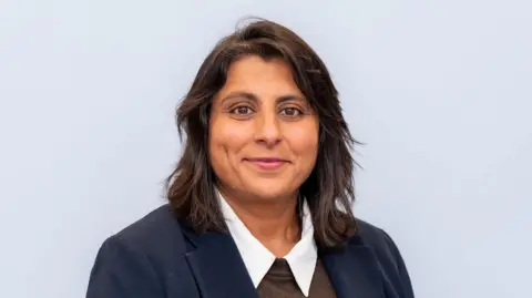 IPPR Avenee wears a navy blazer, white shirt and brown crew-neck jumper. She has shoulder length brown hair and looks straight at the camera.