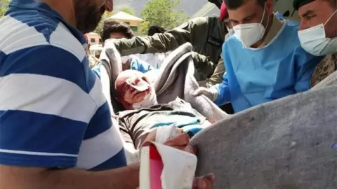 EPA Handout photo shows Pakistani rescue officials shifting an injured person to hospital after a blast at a bus carrying Chinese engineers to the site of Dasu Dam in Kohistan, Pakistan, 14 July 2021.