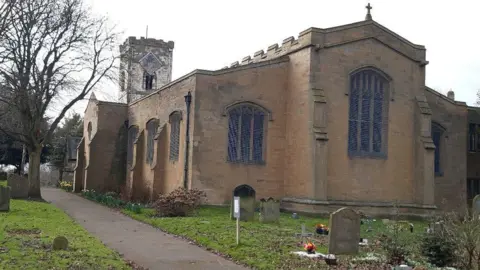 Friends of St Cuthbert's Church Exterior of the 1,000-year-old St Cuthbert's Church which has stained glass windows. There is a green garden with a graveyard in front.