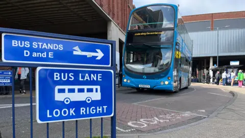 A blue double-decker bus pulling into Great Yarmouth bus station. In the foreground is a blue sign that says "Bus lane – look right"