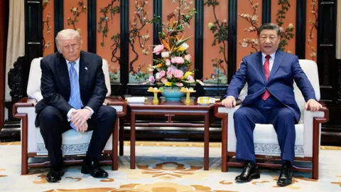 US President Donald Trump (L) and China's President Xi Jinping (R) sit on chairs in a room with ornamental Chinese decorations and furniture